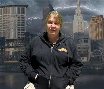 Picture of a blonde woman in a black zip up hoodie in front of a picture of Cleveland during a storm